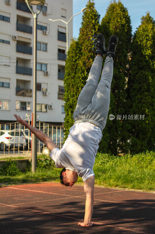 White man doing one hand handstand in a public park